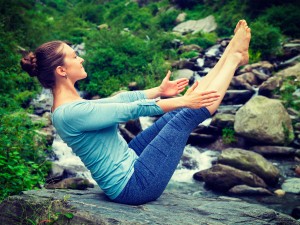 Yoga outdoors - young sporty fit woman doing Ashtanga Vinyasa Yoga asana Navasana - boat pose - in Himalayas at tropical waterfall. Himachal Pradesh, India. Vintage retro effect filtered hipster style image.